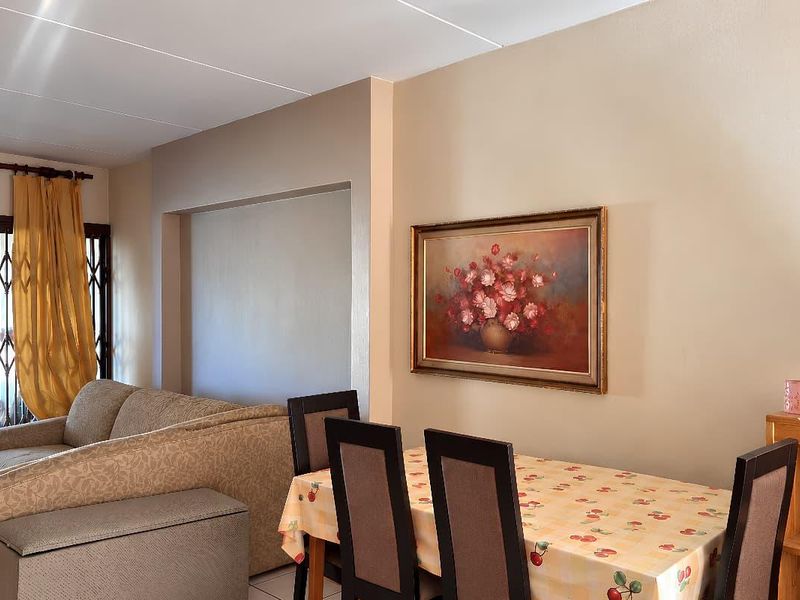 Open plan living and dining area featuring tiled flooring, a recessed wall niche, and access to an outdoor space via a sliding security gate.