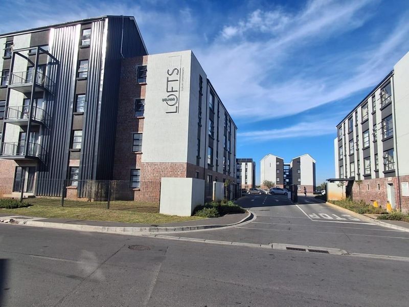 Exterior view of the Delhar Lofts apartment complex featuring modern brick and metal facade architecture with balconies and a secure gated entrance.