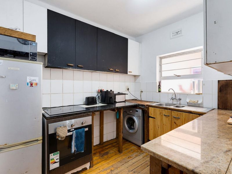 A functional kitchen featuring a built-in oven, electric hob, double sink, and a mix of white and wooden cabinetry with stone countertops.