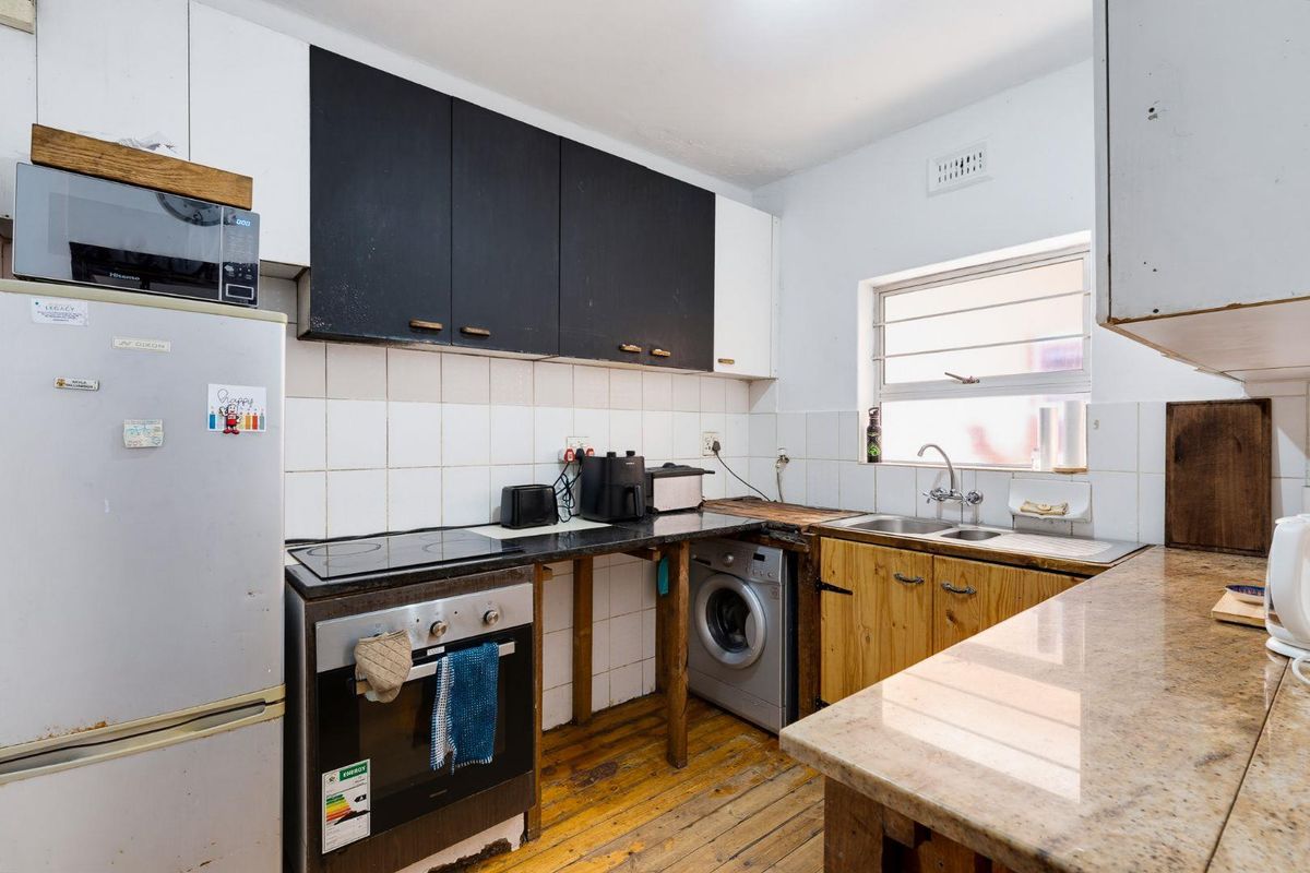 A functional kitchen featuring a built-in oven, electric hob, double sink, and a mix of white and wooden cabinetry with stone countertops.