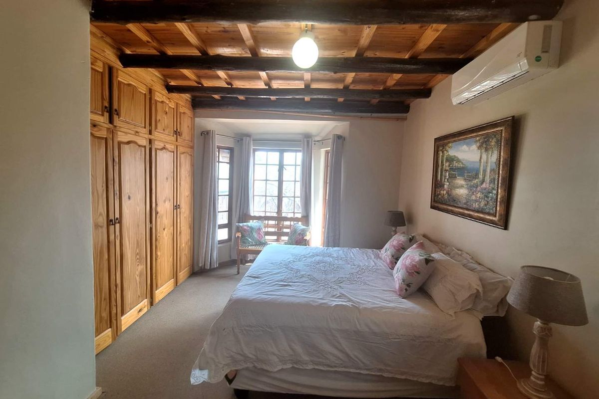 A cozy bedroom featuring exposed timber ceiling beams, built-in wooden cabinetry, and a wall-mounted air conditioning unit.