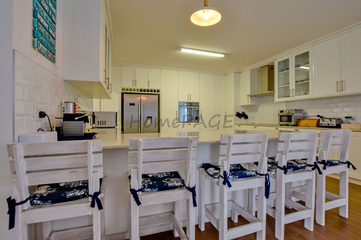 A well-maintained kitchen featuring white cabinetry, stone countertops, subway tile backsplash, and built-in appliances with a breakfast bar island.