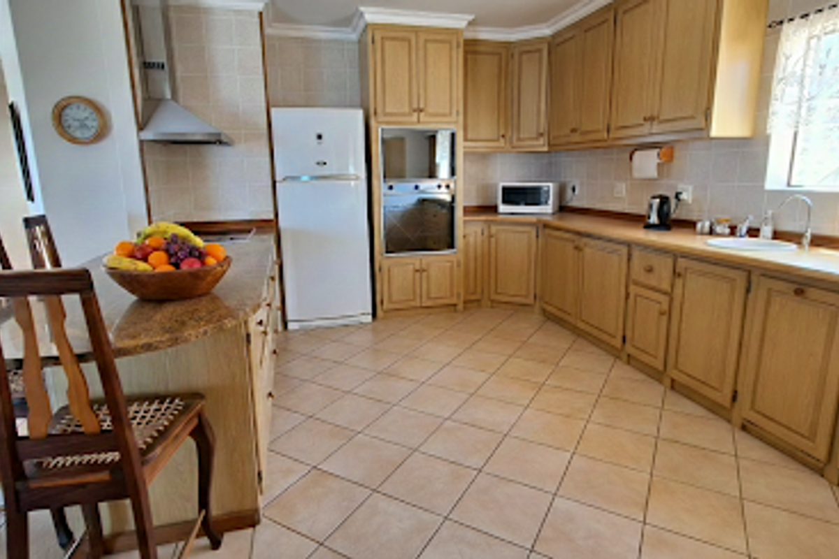 A spacious kitchen featuring light wood cabinetry, granite countertops, a breakfast bar, and tiled flooring, offering a functional layout for cooking and dining.
