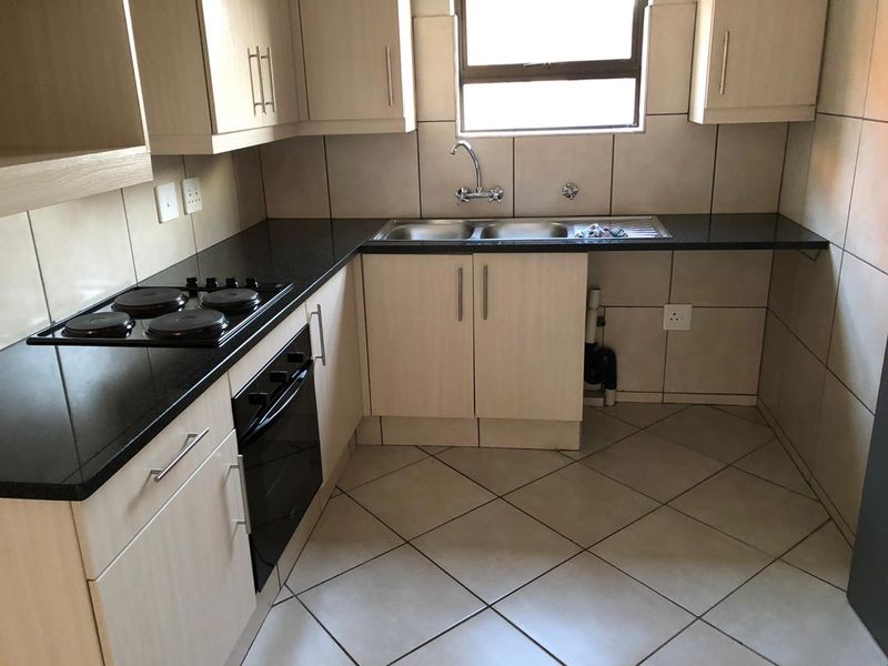 A functional kitchen featuring light wood cabinetry, dark granite countertops, a built-in oven and hob, and tiled finishes throughout.