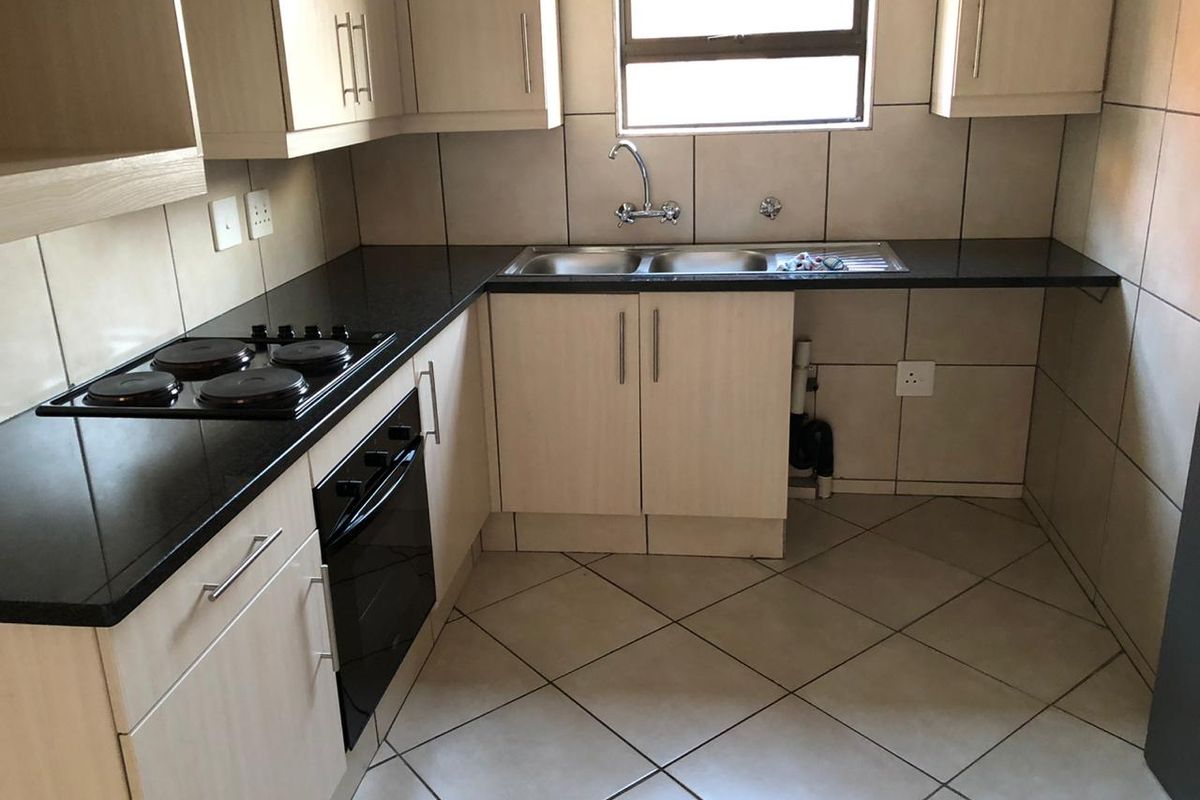 A functional kitchen featuring light wood cabinetry, dark granite countertops, a built-in oven and hob, and tiled finishes throughout.