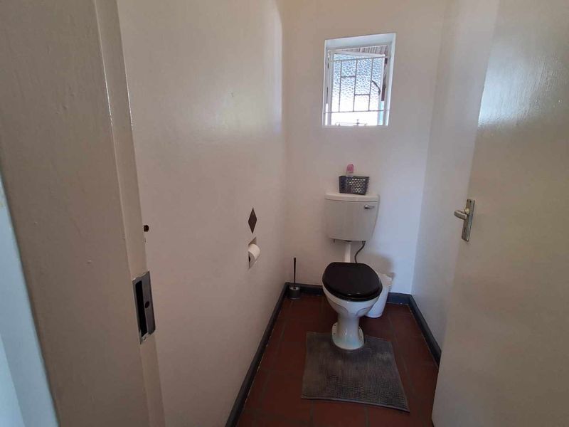 A compact, functional guest toilet featuring tiled flooring and a small casement window, presenting a dated aesthetic in need of cosmetic updates.