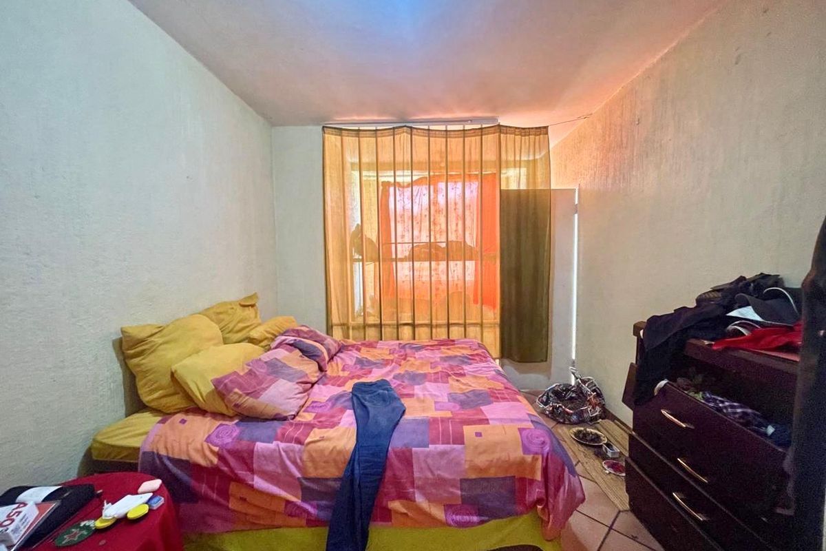 A bedroom featuring tiled flooring and a large window with curtain treatments, providing natural light to the space.