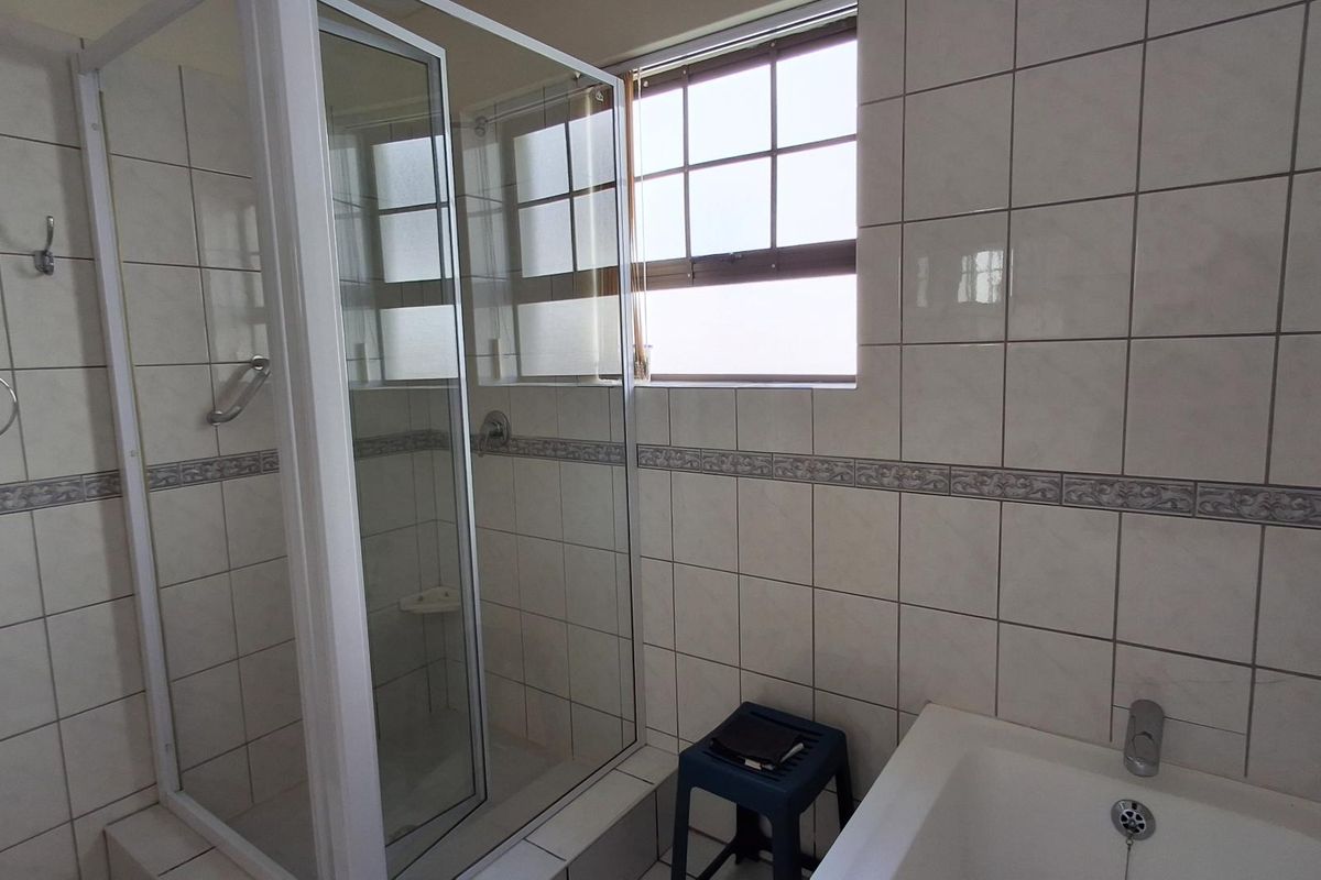 A functional bathroom featuring a shower enclosure, a bathtub, and neutral wall tiling, offering a clean and practical space.