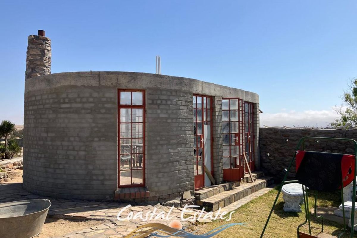 A unique circular structure featuring raw brickwork, a stone chimney, and multiple glass-paned doors, set within a garden area.