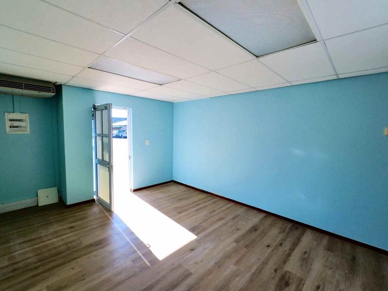 A vacant office space featuring laminate flooring, a suspended ceiling, and a wall-mounted air conditioning unit with direct exterior access.