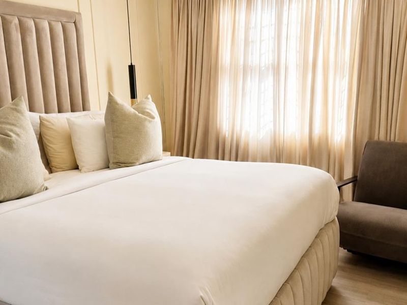 A well-maintained bedroom featuring neutral wall paneling, laminate flooring, and floor-to-ceiling curtains, creating a warm and inviting atmosphere.
