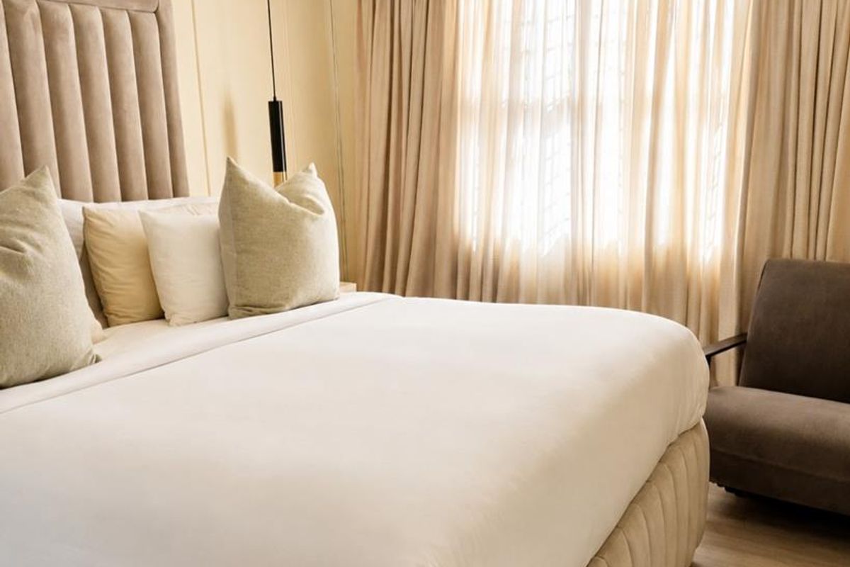 A well-maintained bedroom featuring neutral wall paneling, laminate flooring, and floor-to-ceiling curtains, creating a warm and inviting atmosphere.