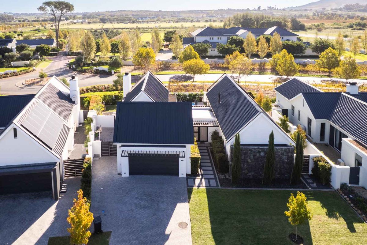 Aerial view of a modern residential property featuring a metal roof, solar panels, stone accents, and a paved driveway within a landscaped estate.