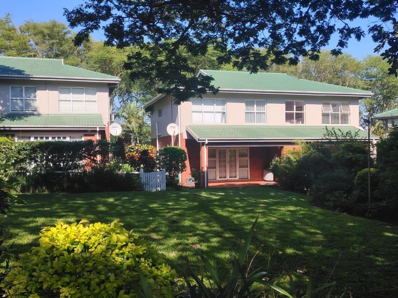 Rear view of a two-story apartment building featuring a green tiled roof, brick exterior, and a covered patio overlooking a private garden.