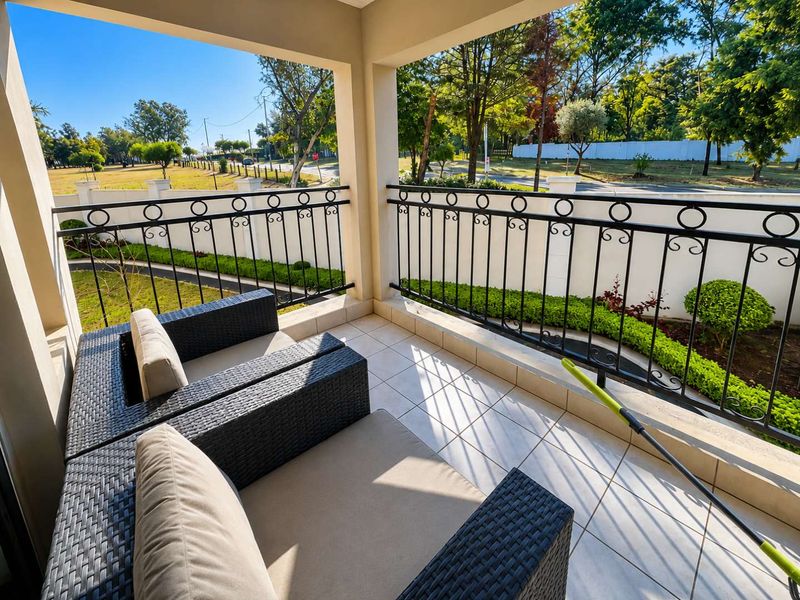 A covered balcony featuring tiled flooring and a decorative wrought iron balustrade, overlooking a landscaped garden area.