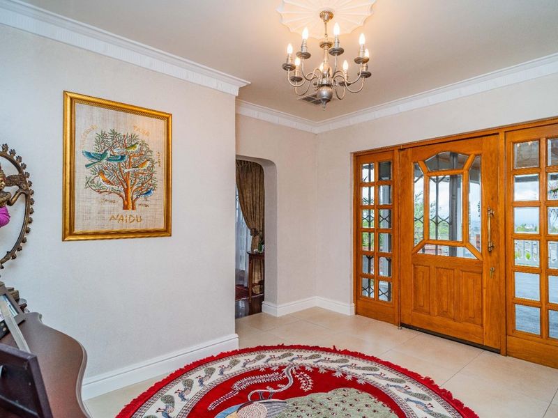 Welcoming entrance hall featuring a solid timber front door with glass sidelights, elegant ceiling rose with chandelier, and neutral tiled flooring.