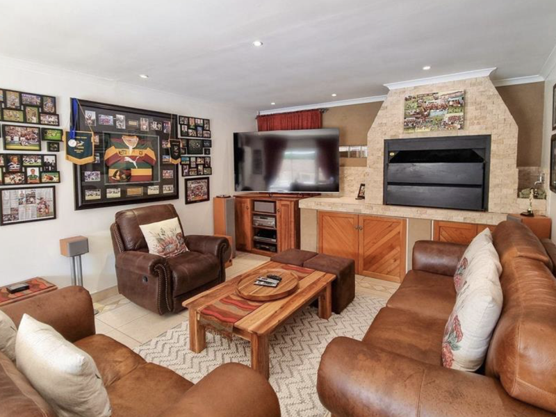 A comfortable living room featuring a prominent stone-clad built-in fireplace, tiled flooring, and recessed lighting, creating a warm and inviting atmosphere.