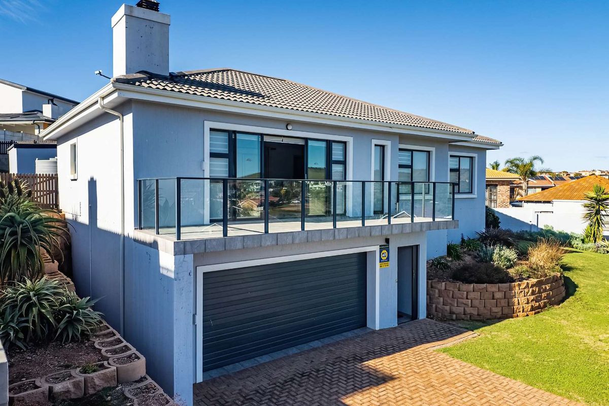 Rear exterior view of the house featuring a balcony with glass balustrade, a paved driveway, and a lower-level garage.