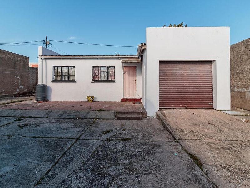 Rear exterior view of the office property featuring a concrete driveway, a roller garage door, and a perimeter boundary wall.