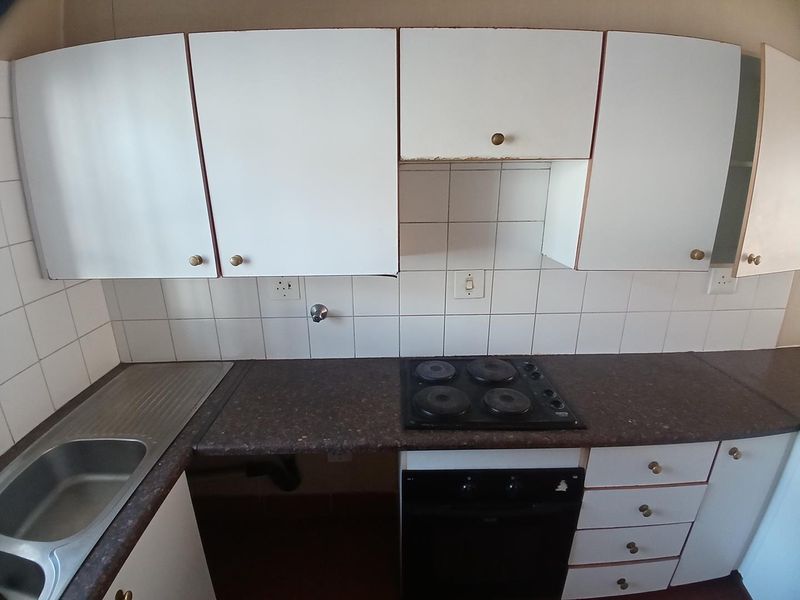 A compact kitchen featuring white cabinetry, dark laminate countertops, a built-in oven with electric hob, and a stainless steel sink with tiled backsplash.