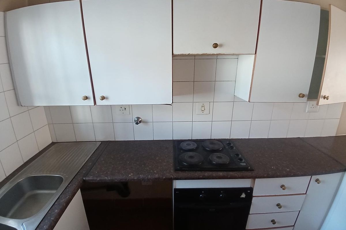 A compact kitchen featuring white cabinetry, dark laminate countertops, a built-in oven with electric hob, and a stainless steel sink with tiled backsplash.