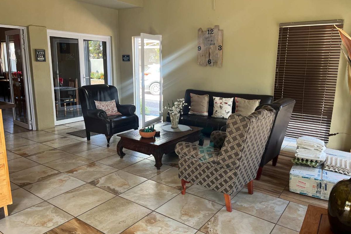 A spacious living area featuring large ceramic floor tiles, multiple glass-paneled doors providing natural light, and integrated window blinds.