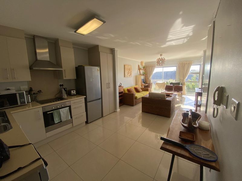 Open-plan living area featuring a modern kitchen with built-in appliances, tiled flooring, and a bright lounge area leading to a balcony.