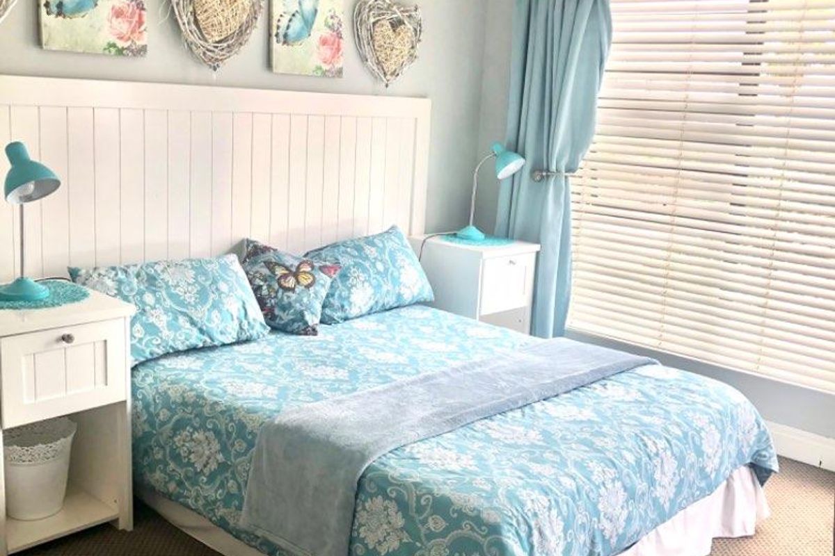 A cozy bedroom featuring a built-in white headboard, neutral carpeting, and venetian blinds, offering a bright and functional living space.