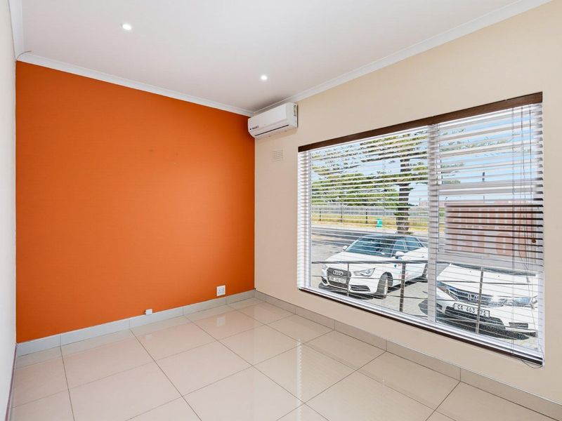 A bright, empty office space featuring tiled flooring, an air conditioning unit, and large windows with venetian blinds.
