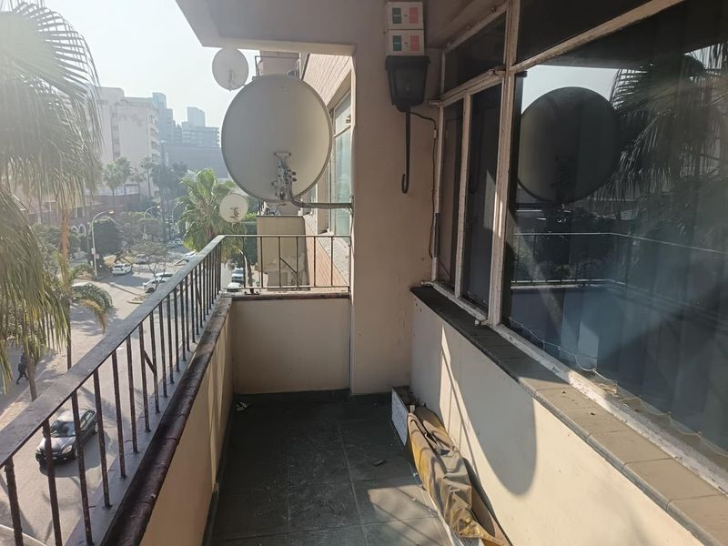 A balcony area featuring tiled flooring and a metal balustrade, offering an urban street view.