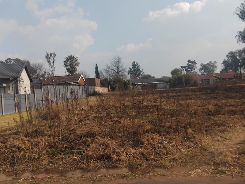 A vacant residential plot featuring a concrete boundary wall and direct access to a paved road, ready for development.