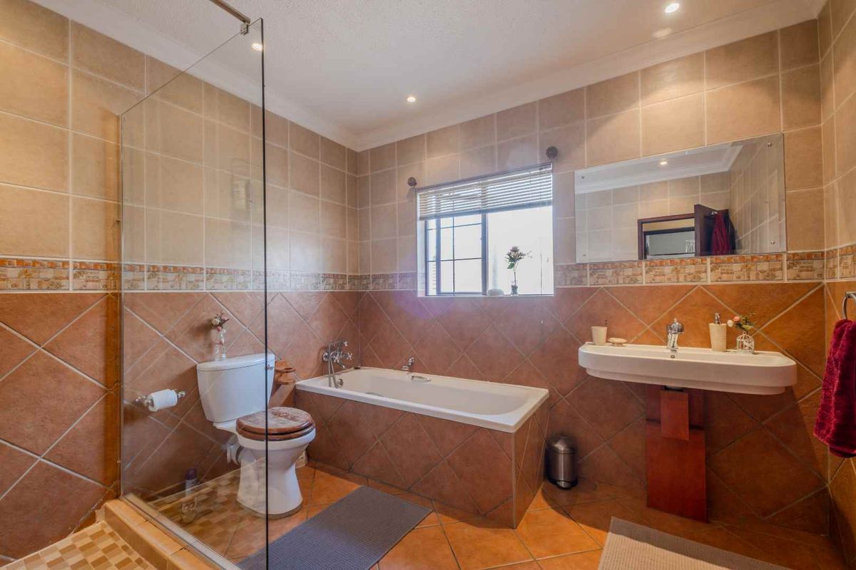 A functional bathroom featuring a glass-enclosed shower, a built-in bathtub, a pedestal sink, and tiled walls and flooring.