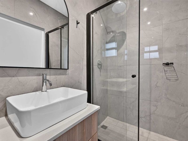 Modern bathroom featuring a vessel sink on a vanity cabinet, a glass-enclosed shower, and contemporary grey wall tiling.