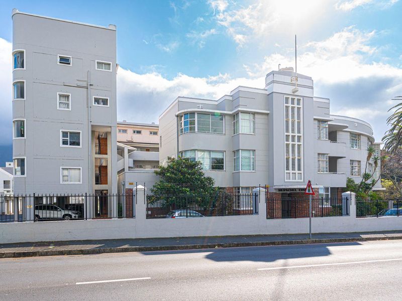 Front elevation of a well-maintained Art Deco style apartment building featuring a masonry boundary wall and secure wrought iron perimeter fencing.