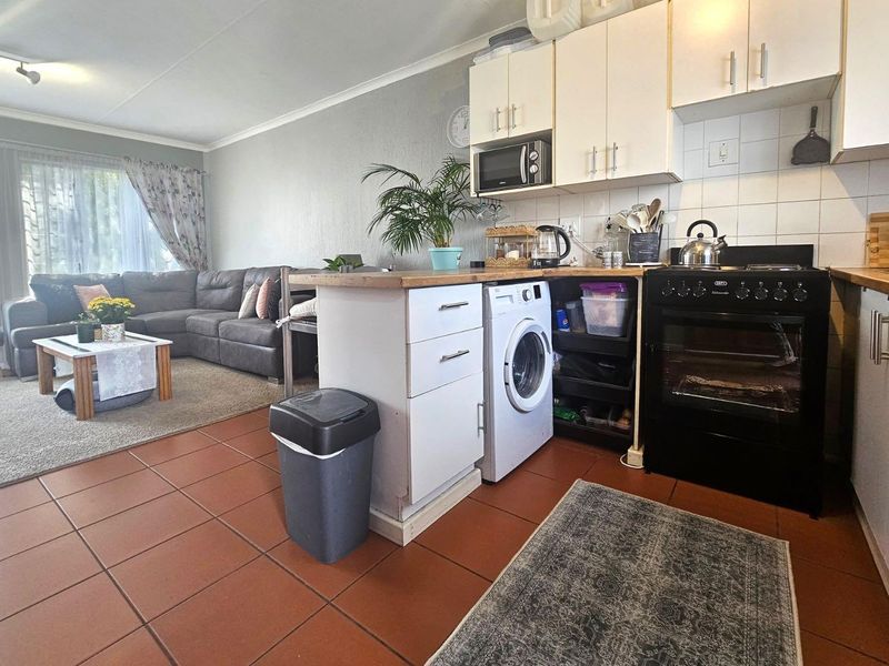 Open-plan living area featuring a functional kitchen with built-in cabinetry, tiled flooring, and integrated laundry plumbing, seamlessly connected to the lounge space.