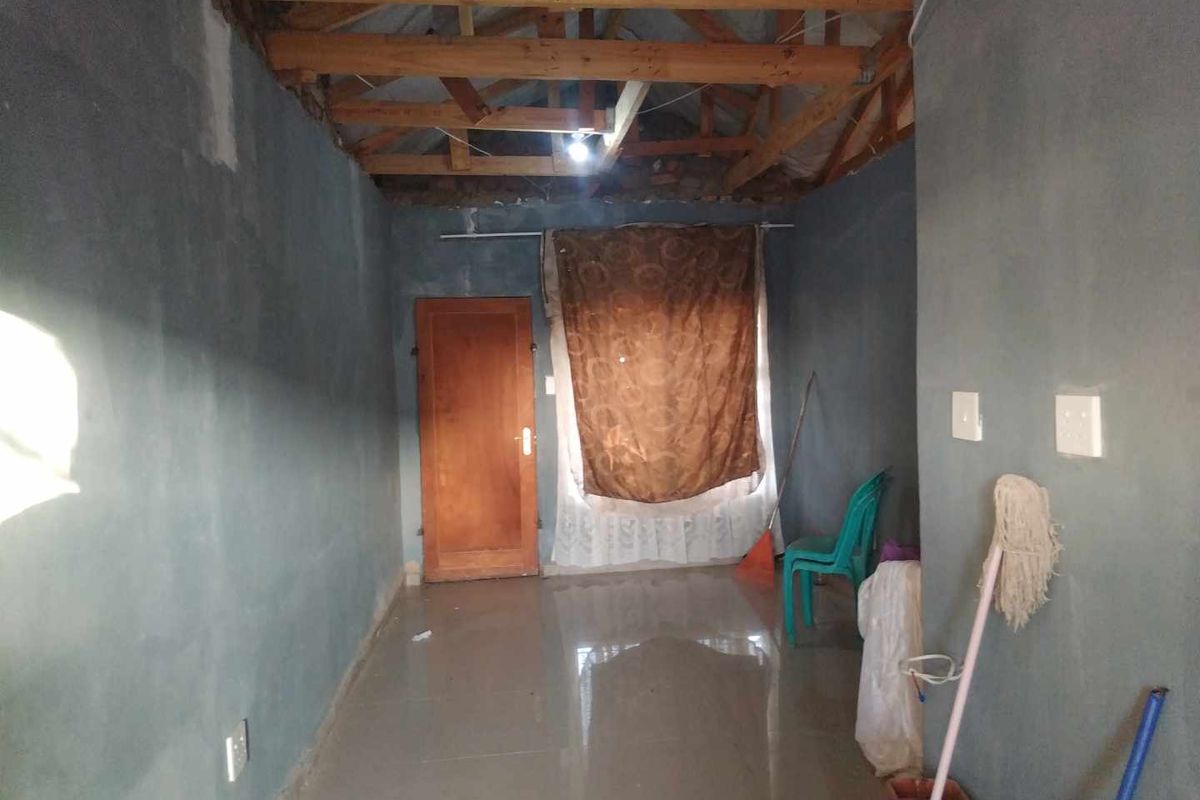 An unfinished interior room featuring exposed timber roof trusses, tiled flooring, and a single wooden door.
