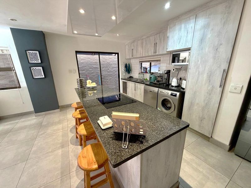 Modern kitchen featuring a large granite-topped island with integrated induction hob, light wood-grain cabinetry, subway tile backsplash, and recessed ceiling lighting.