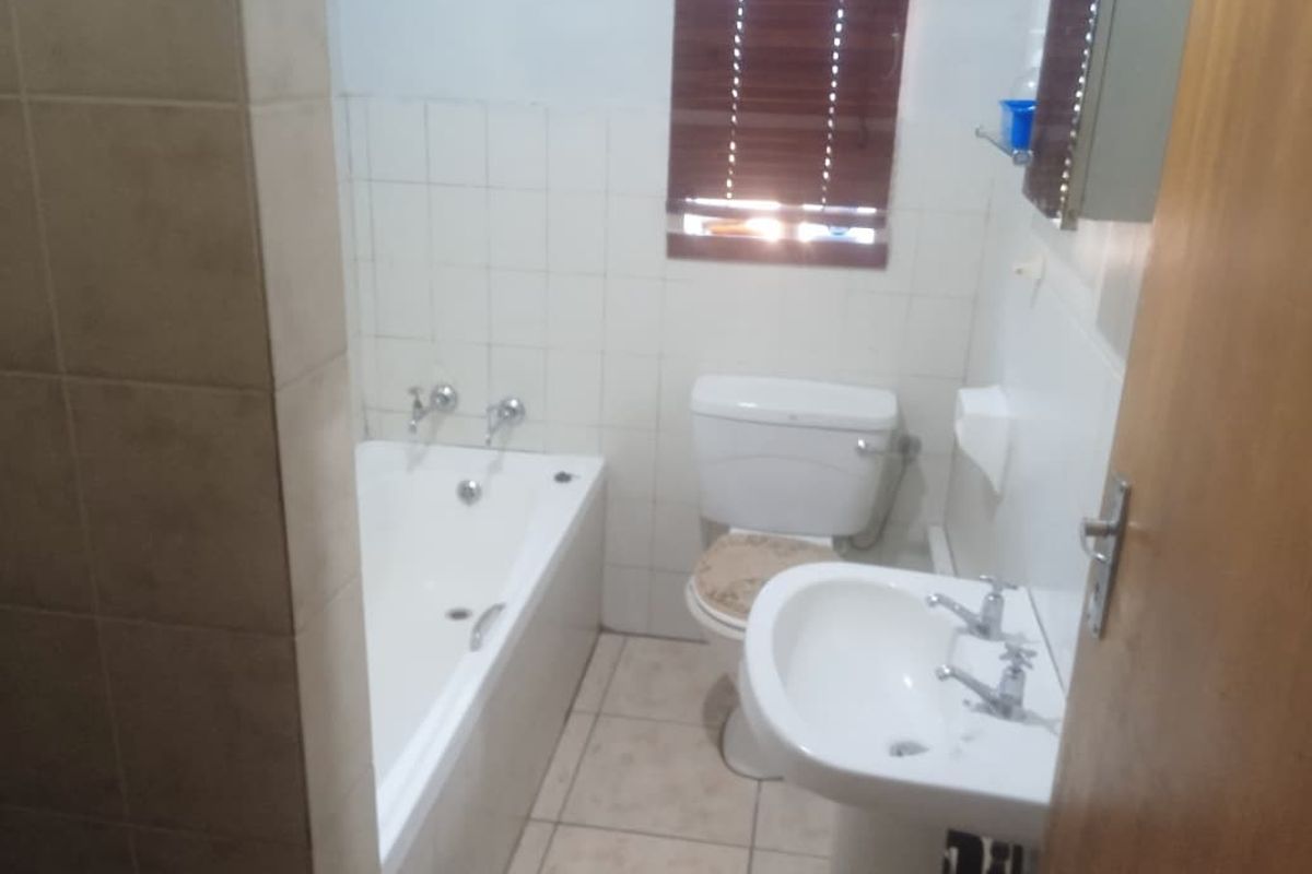 A functional bathroom featuring a built-in bathtub, pedestal basin, and toilet, finished with neutral wall and floor tiling.