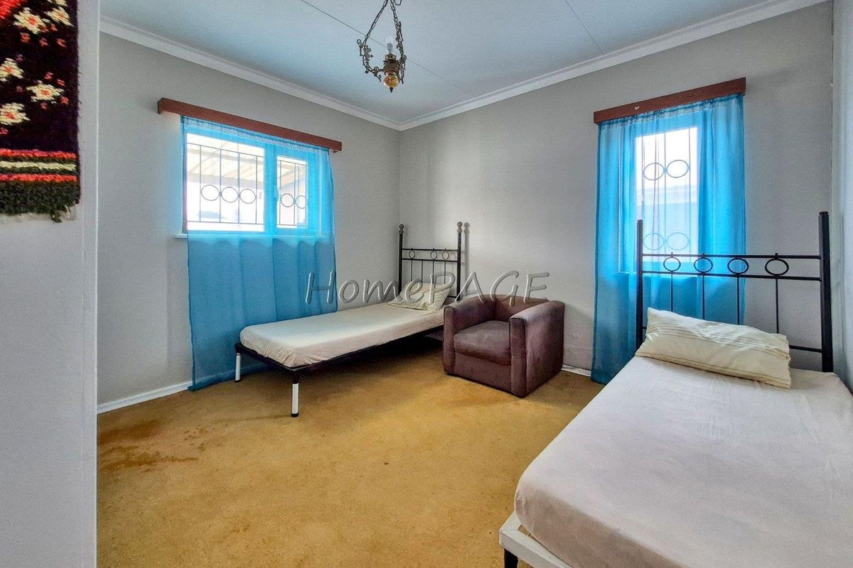 A bedroom featuring two single beds, carpeted flooring, and two windows with security bars.