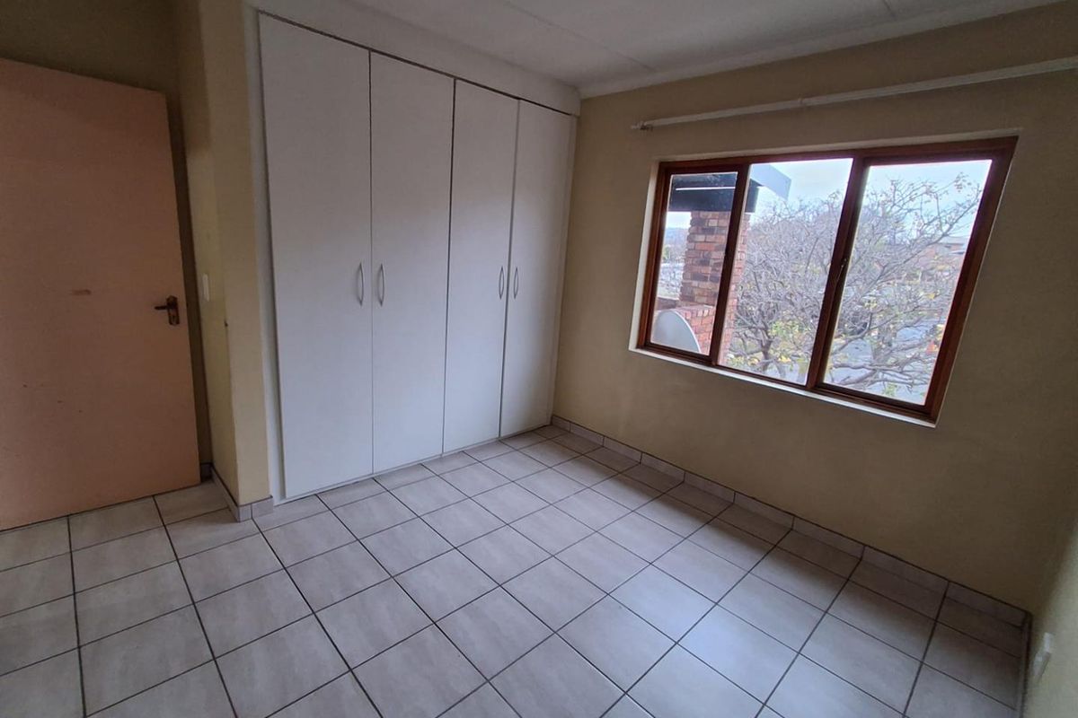 A vacant bedroom featuring neutral floor tiles, built-in white cupboards, and a window providing natural light.