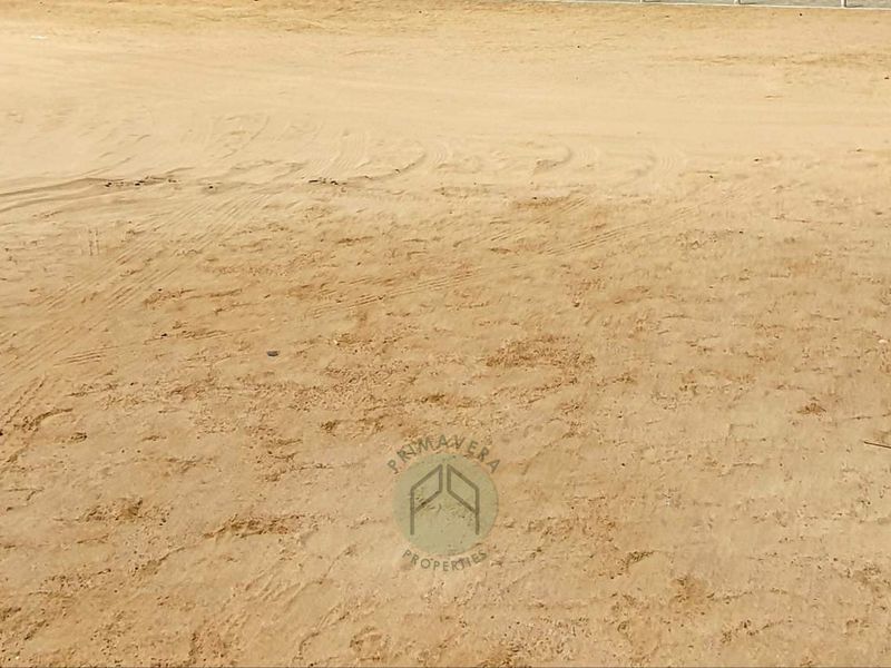 A view of a vacant residential plot of land with sandy terrain.
