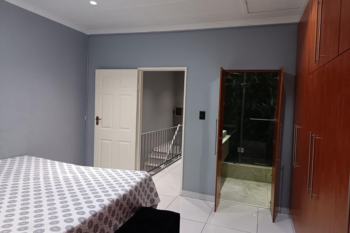 A well-maintained bedroom featuring built-in wooden cupboards, tiled flooring, recessed lighting, and direct access to an en-suite bathroom and hallway.