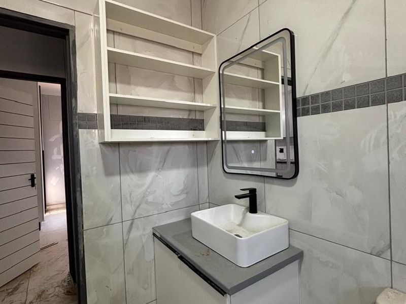 A modern bathroom featuring marble-look wall tiles, a vanity with a vessel sink, black fixtures, and built-in shelving, currently undergoing final finishing touches.