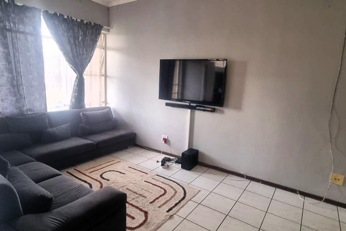 A living room featuring tiled flooring, large windows with curtains, and a wall-mounted television setup.