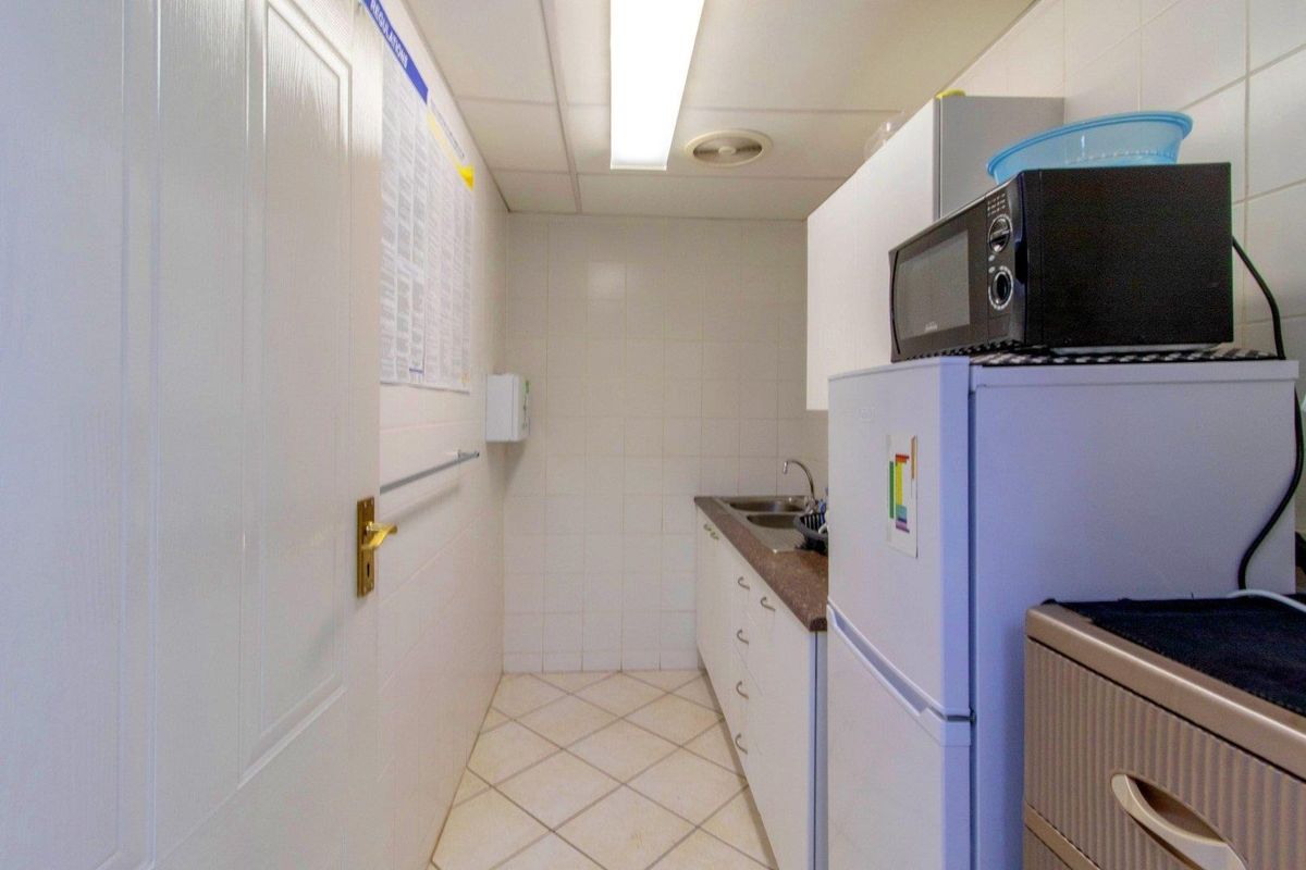 A functional kitchenette area featuring tiled walls, tiled flooring, built-in cabinetry, and a stainless steel sink.