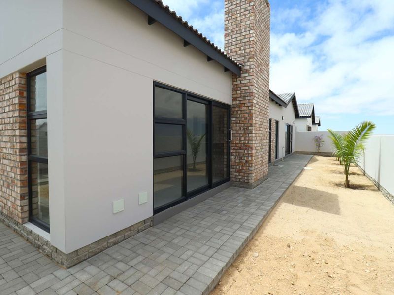 Rear exterior view of the house featuring a brick chimney, paved walkway, and modern sliding glass doors leading into the living area.