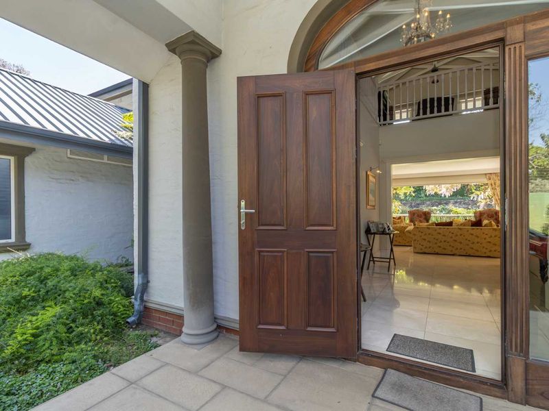 Inviting entrance featuring a solid timber door, arched transom window, and stone-paved patio, leading into a bright, open-plan living space with tiled floors.
