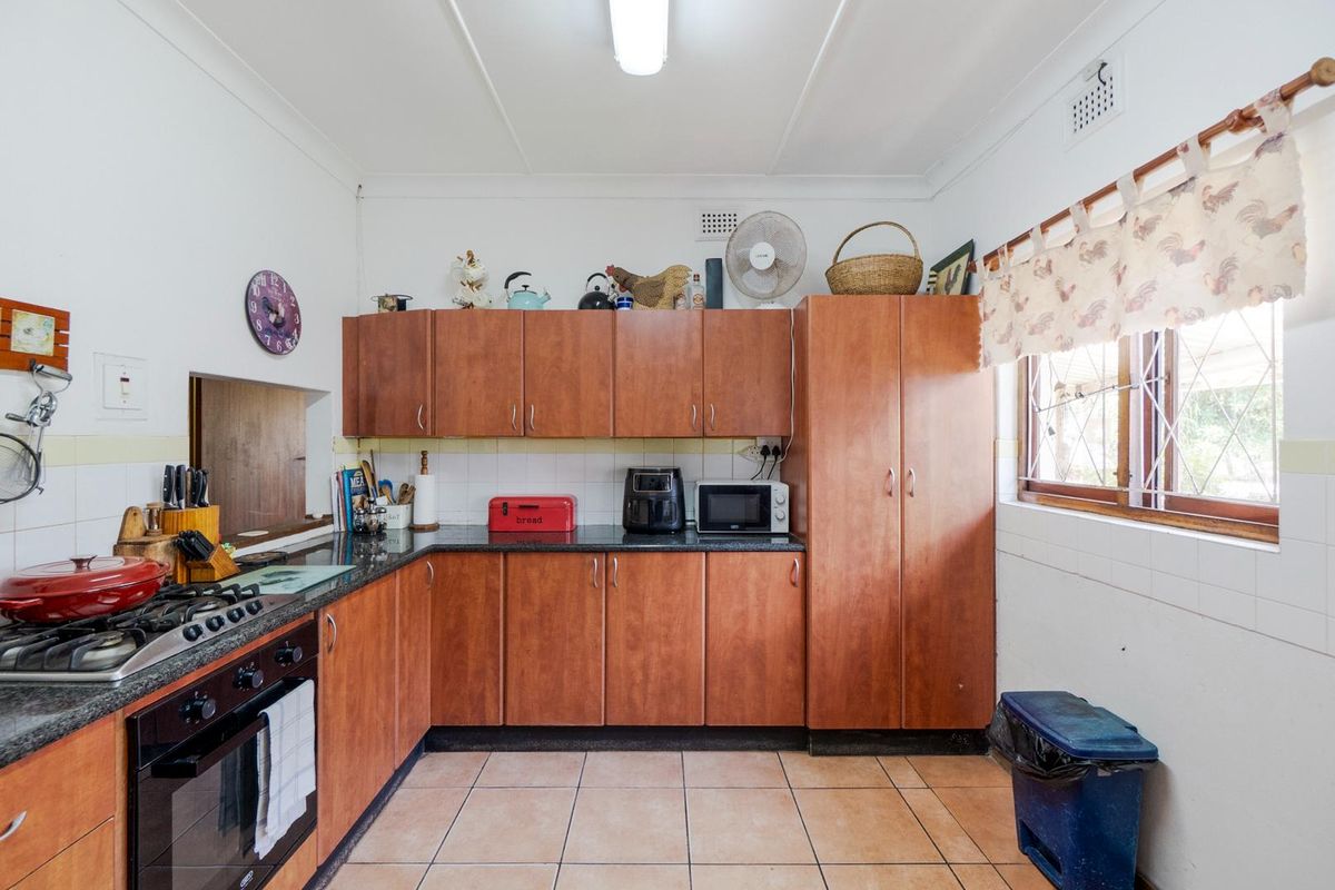 A functional kitchen featuring wooden cabinetry, granite countertops, a built-in oven, and a gas hob, with tiled flooring and walls.