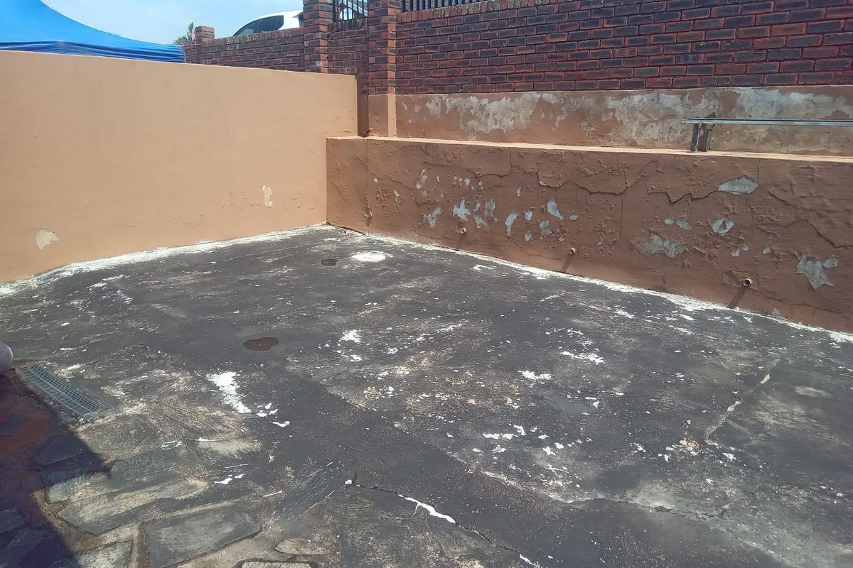 A rear outdoor area featuring a paved surface and a retaining wall with visible signs of weathering and paint deterioration.