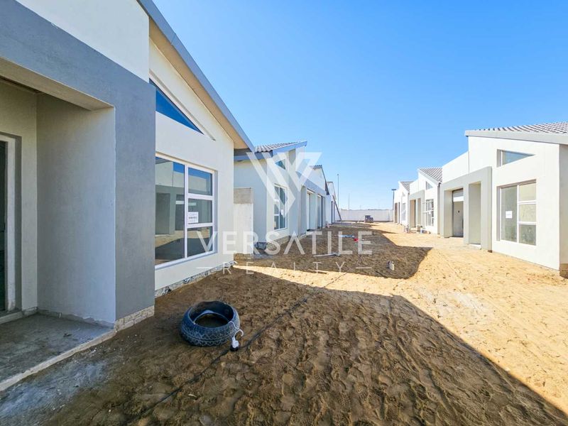 Exterior view of a townhouse development showing unfinished ground and modern plastered facades with aluminium window frames.